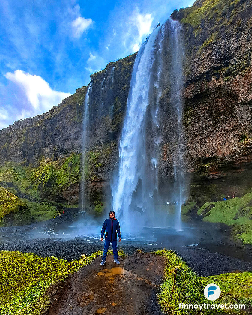Ceasar standing in front of the tall Seljalandfoss Waterfall in Iceland